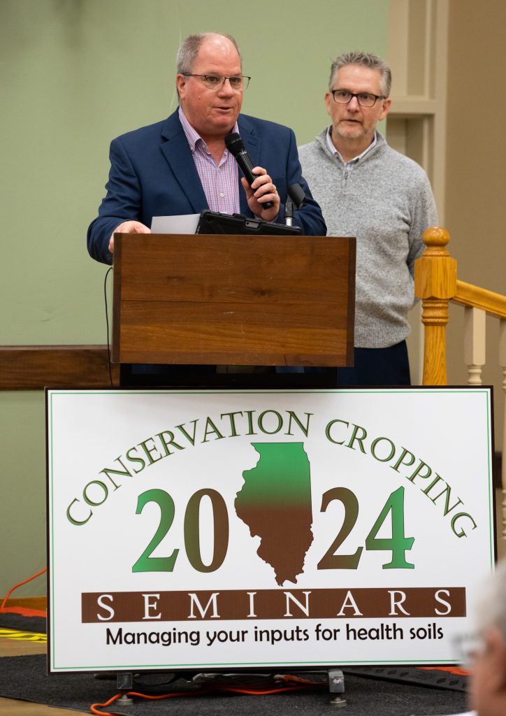 Todd Gleason and Dr. Michael Woods at podium with 2024 Conservation Cropping Seminar sign.