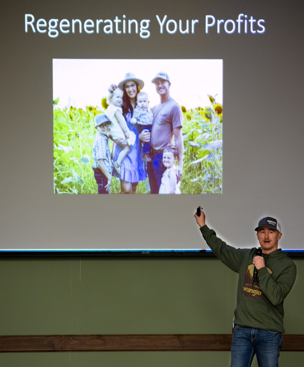 Macauley Kincaid points as he stands in front of a screen featuring an image of his family in a field of sunflowers.