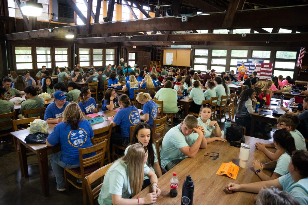 Packed dining hall, with student teams sitting at tables.